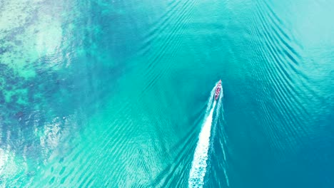 Boat-sailing-across-calm-clear-water-of-blue-turquoise-sea-reflecting-sunlight-near-shore-of-tropical-island-in-Malaysia