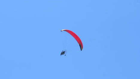 unrecognizable person flying by paramotor against blue sky