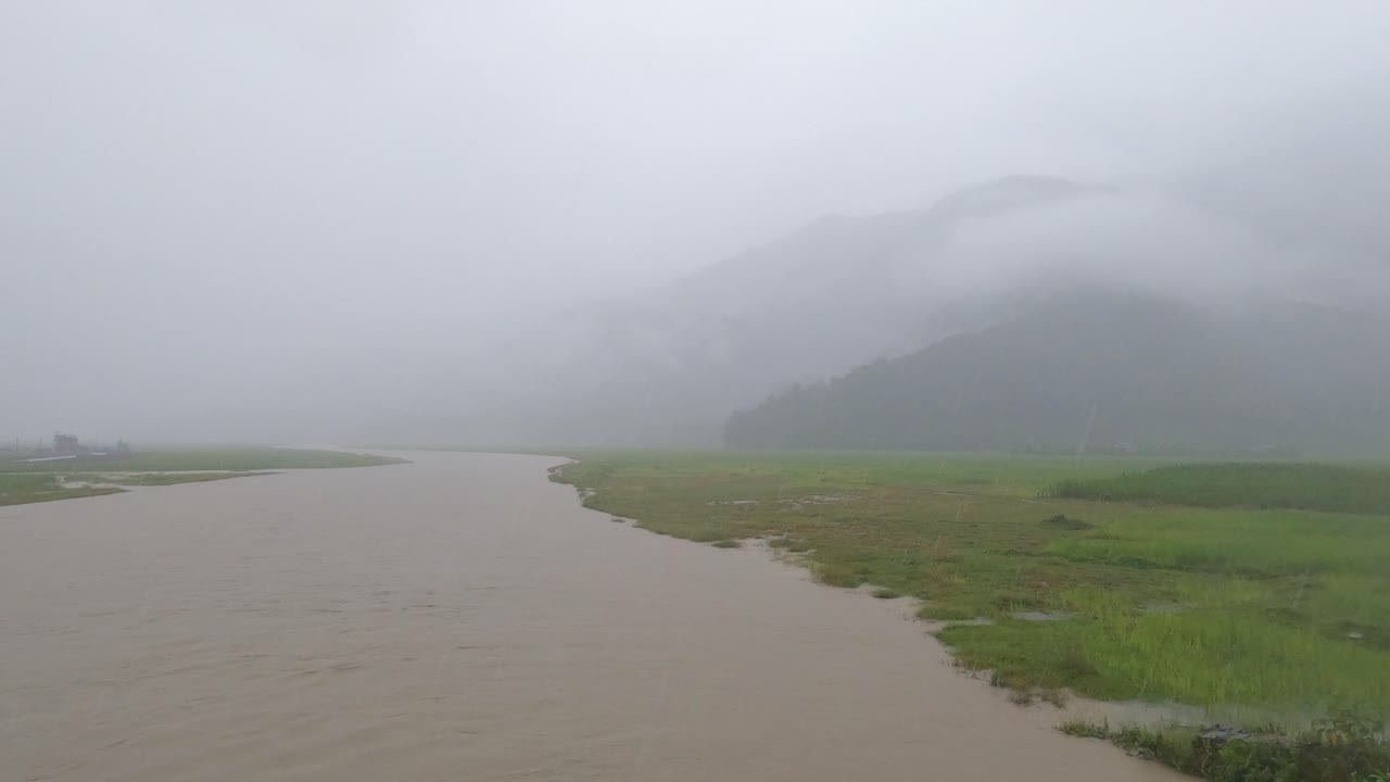 네팔의 몬순 기간 동안 범람한 강을 바라보며 폭우 속에서 다리에 서 있다