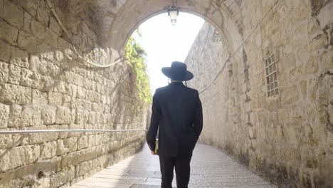 a man in traditional attire walks through a sunlit stone archway, moving from shadow into light