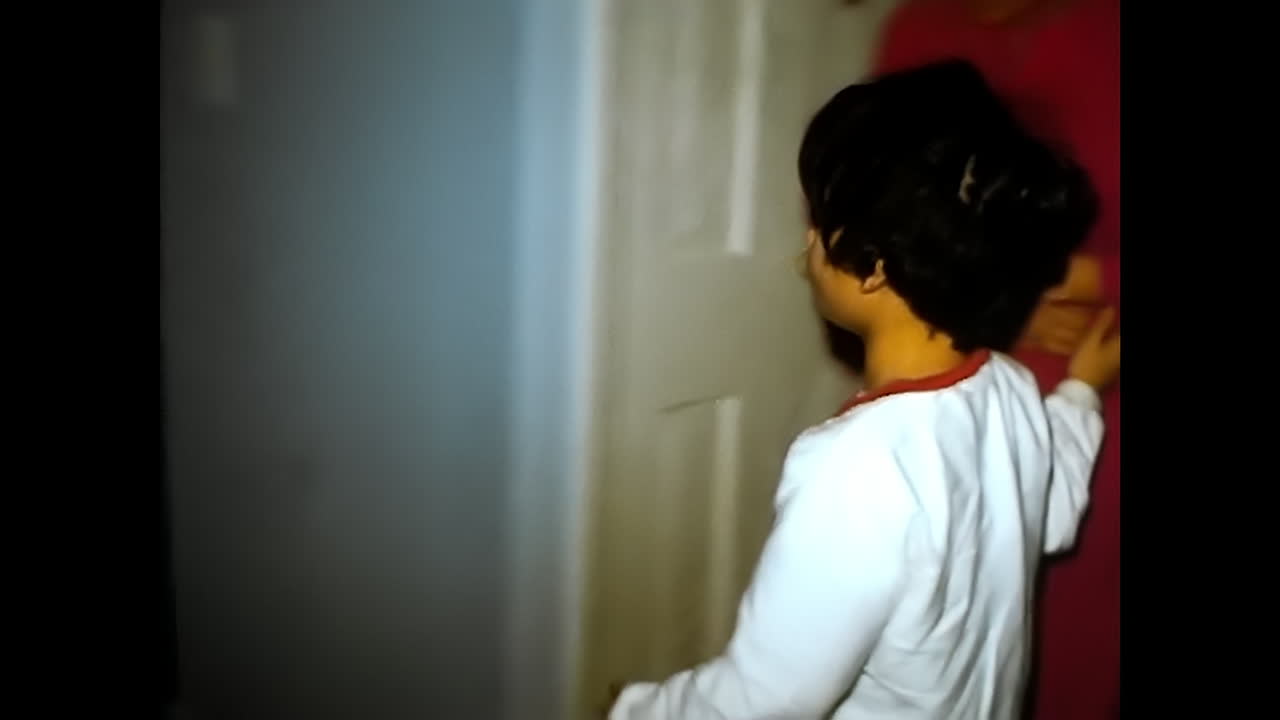 Little Boy and Woman Standing by Christmas Tree. CIRCA USA - 1970s: A little boy stands next to a woman in front of a Christmas tree, captured in a 1970s video archive from the USA.