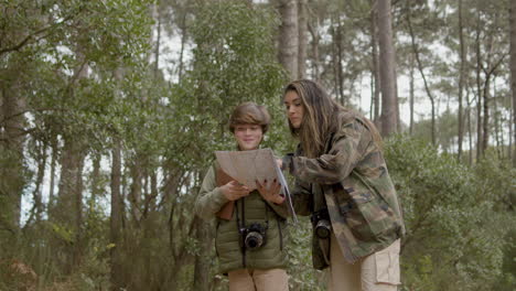 caucasian woman and her son in a natural park looking at paper map to find their way, then woman showing direction