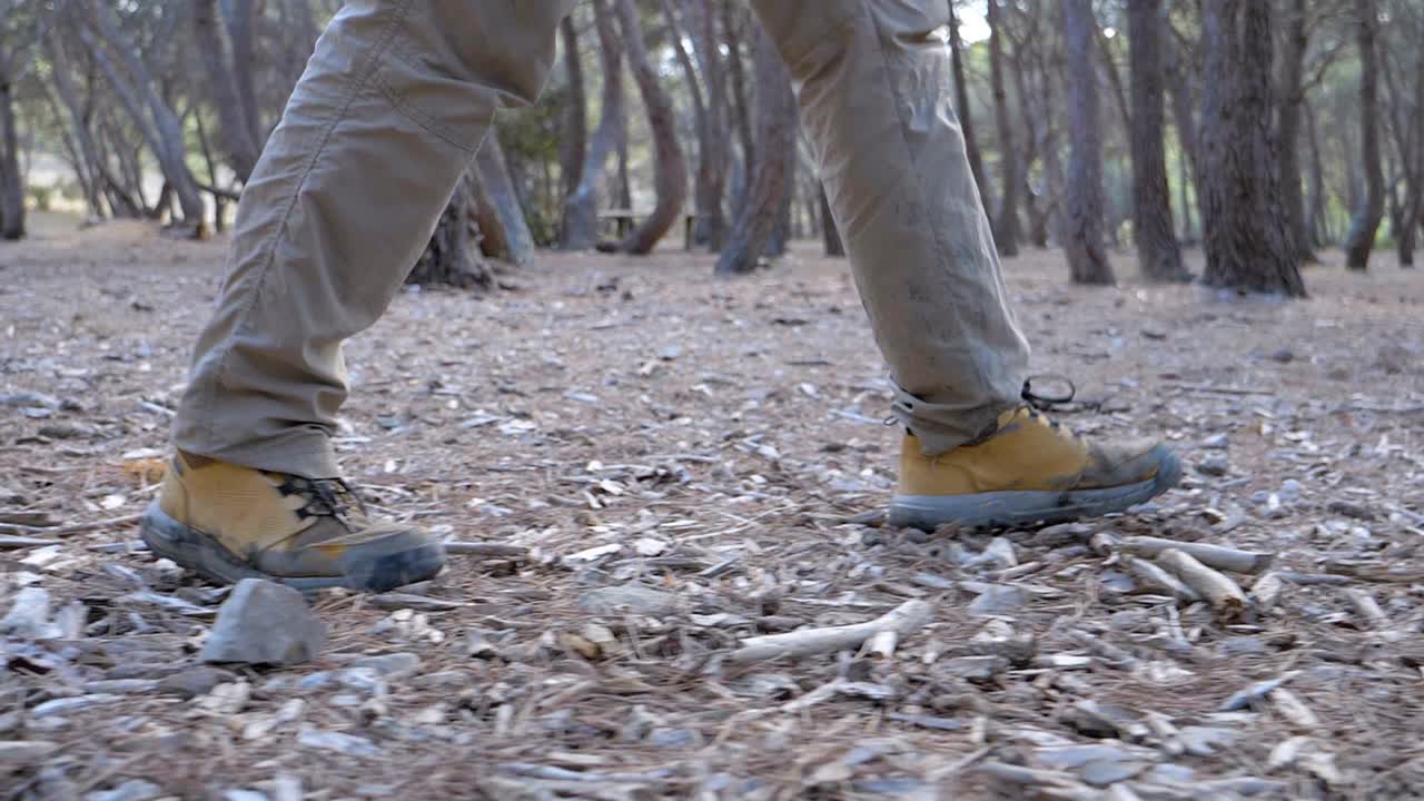 Slow motion low angle shot of a man's boots walking through a wooded area over sticks