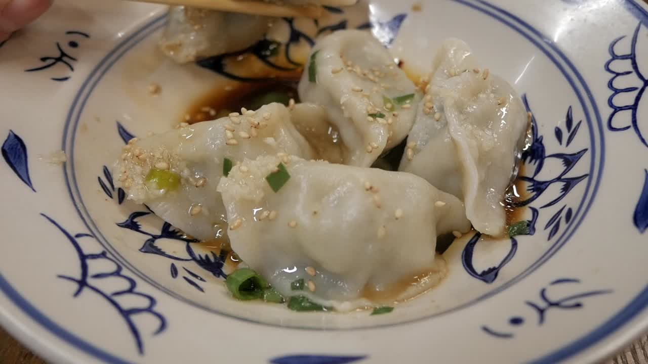 Chopsticks pick delicious dumplings from blue floral bowl, soy sauce drizzle
