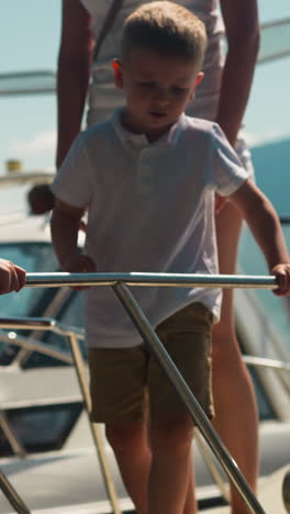 little girl carefully goes down motorboat ladder while mother and boy wait on drawbridge landing in city port. elder sister shows brother landing from yacht