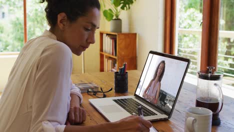 Mujer-Afroamericana-Tomando-Notas-Mientras-Realiza-Una-Videollamada-En-Una-Computadora-Portátil-En-Casa