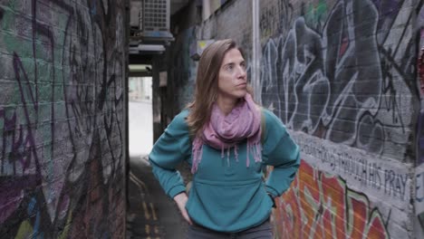 young woman walks in a narrow alley with walls painted with graffiti