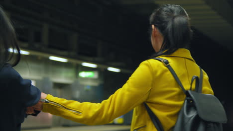 Two-Young-Female-Friends-Holding-Hands-As-They-Say-Goodbye-On-Underground-Train-Station-Platform