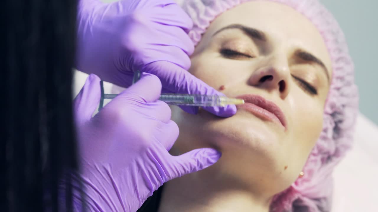 Cosmetologist makes lip augmentation procedure with syringe of a beautiful woman in beauty salon.Cosmetology skin care
