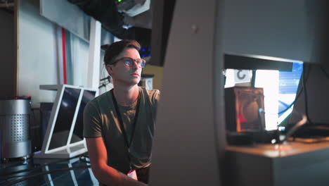 a person sitting on the studio floor, adjusting equipment while focused on the screen in front. studio lights and cameras are visible in the background, creating a busy production environment
