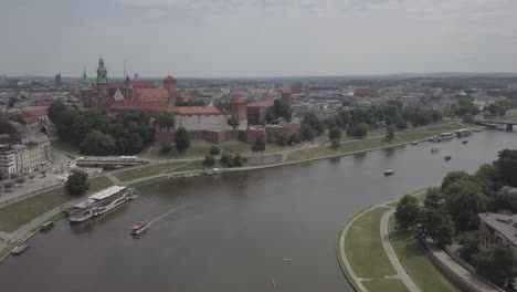 Poland,-Krakow-drone-shot-zooming-in-from-the-front-of-the-Castle-Wawel-with-Wisla-in-foreground-and-buildings-in-the-background