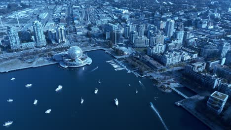 Science-World-False-Creek-Olympic-Village-aerial-flyover-yachts-mooring-over-reflective-blue-water-mirroring-iconic-modern-buildings-bords-top-view-overlooking-Main-Street-connection-to-Downtown-East