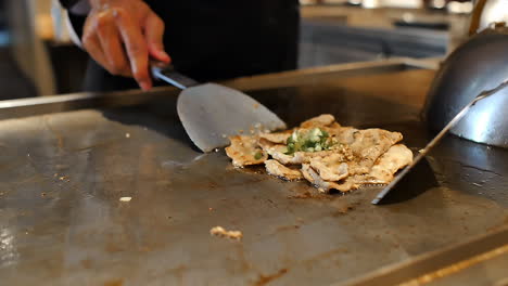 close-up of a skilled chef preparing teppanyaki japanese cuisine on a hot iron griddle in front of guests, grilling fresh ingredients with flair. perfect for japanese food culture and live cooking
