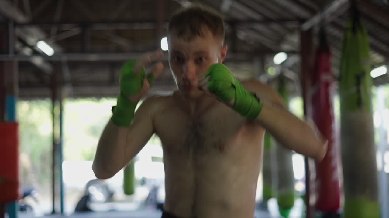 Man training Muay Thai or boxing in a gym, practicing punches and wiping sweat