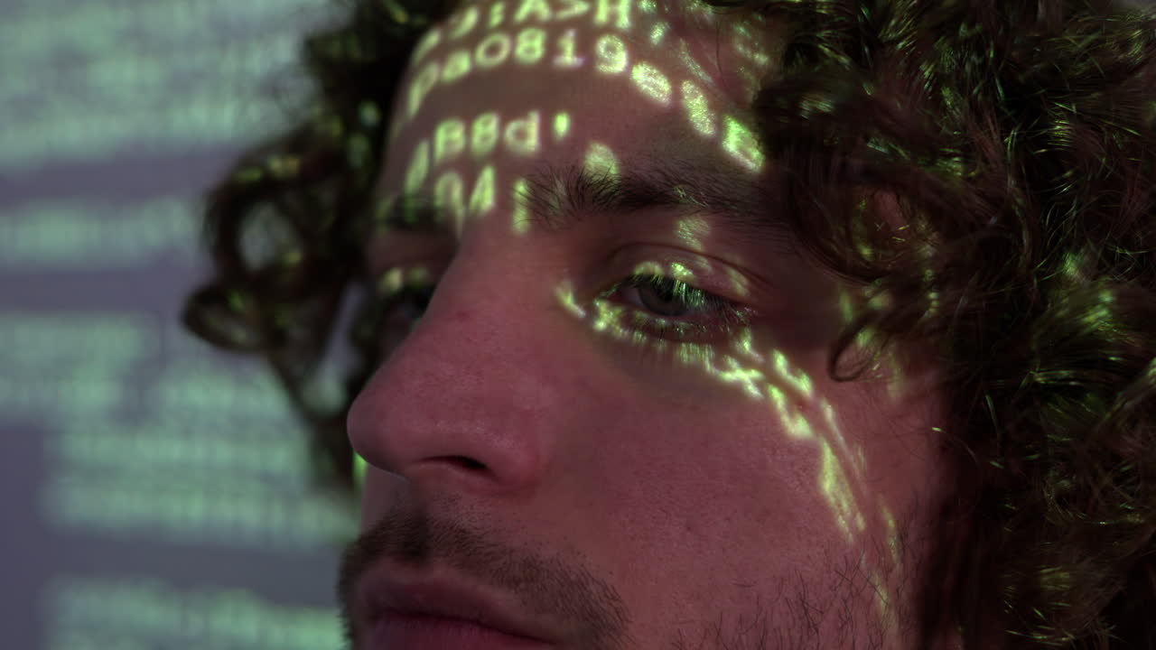 Uomo con i capelli ricci davanti a una proiezione di codice informatico verde che illumina il suo volto
