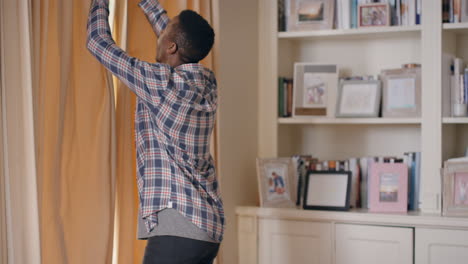 happy-african-american-man-opening-curtains-looking-out-window-enjoying-bright-sunny-new-day-smiling-cheerfully-at-home-on-weekend-morning-4k