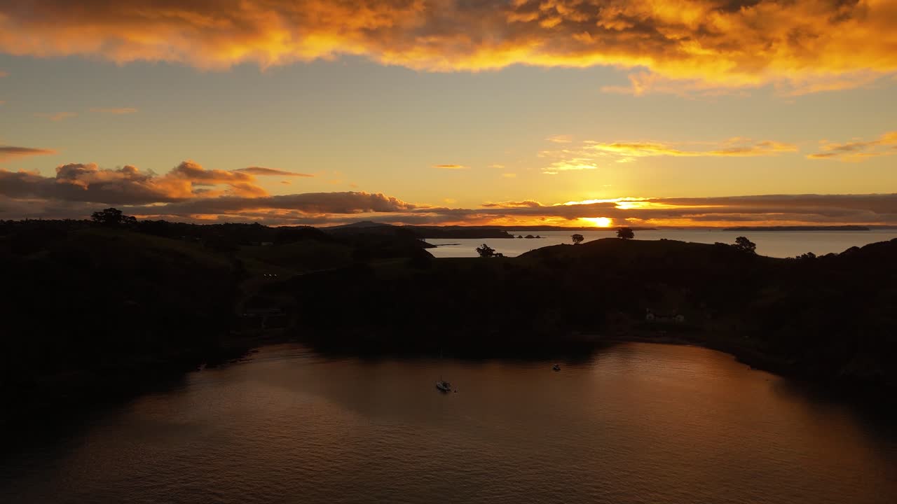 Golden hour with golden clouds at horizon of ocean in New Zealand. Cliffs and hills Silhouette in the evening. Aerial wide shot.
