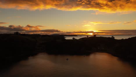 golden hour with golden clouds at horizon of ocean in new zealand. cliffs and hills silhouette in the evening. aerial wide shot.
