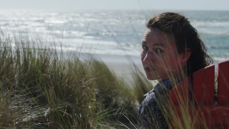 a woman sits in a chair at the coast and turns to look into the camera