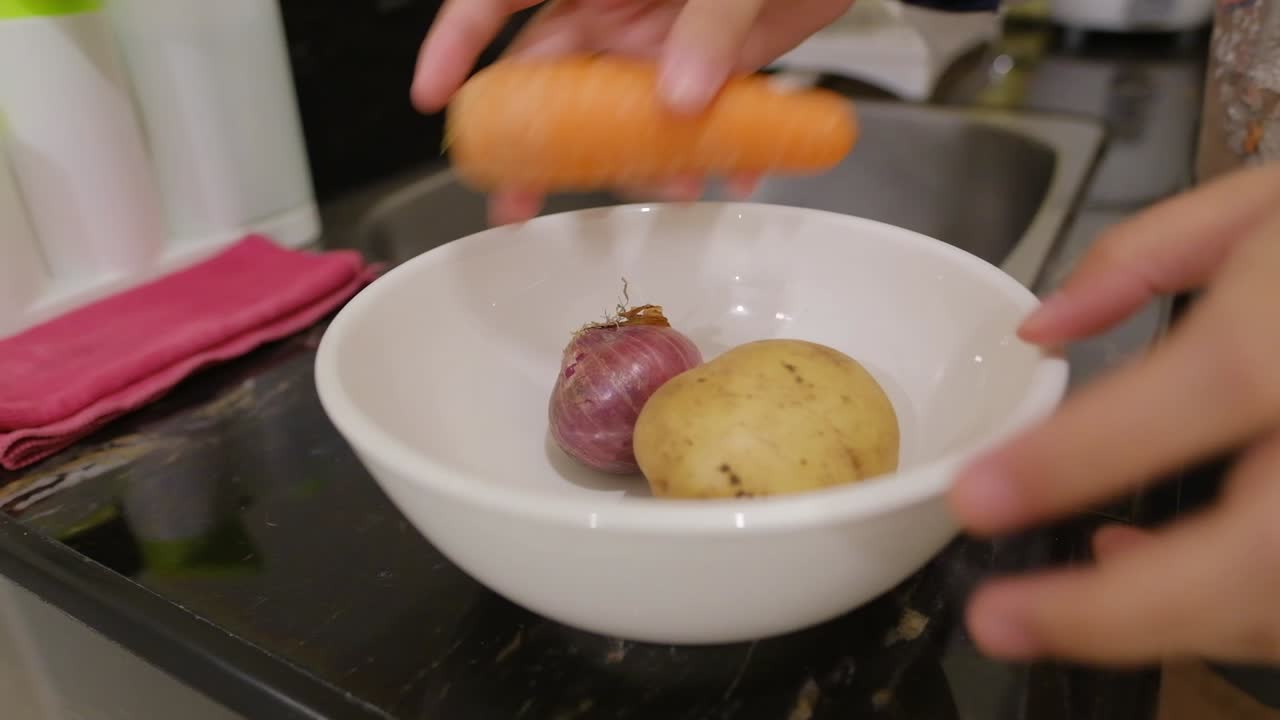 Person Places Fresh Raw Potato, Red Onion, And Carrot In White Ceramic Bowl For Washing In The Kitchen Sink