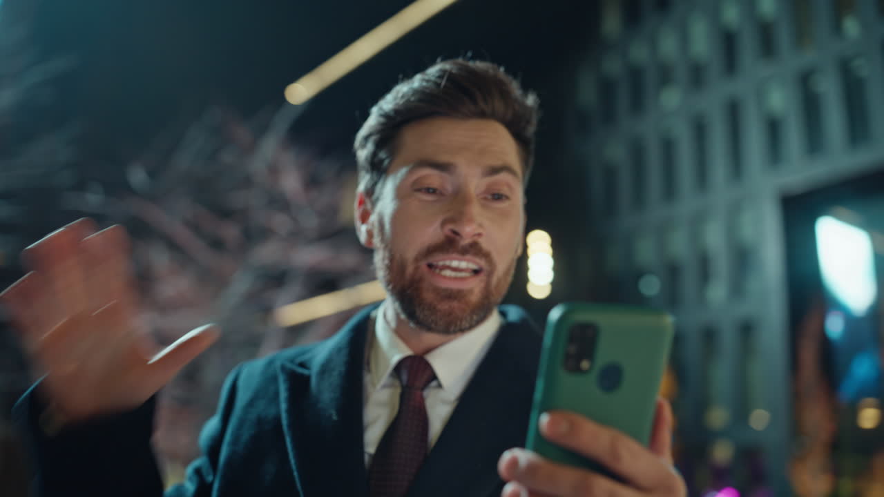 Emotional businessman talking videocall at smartphone in evening city closeup