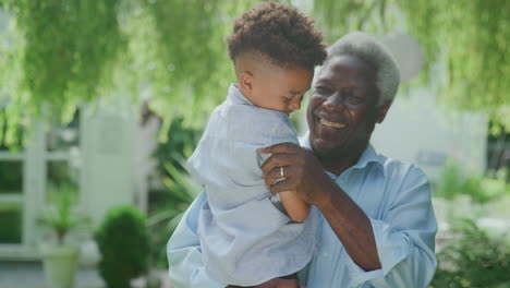 Loving-Grandfather-Holding-Grandson-In-Arms-In-Garden-At-Home