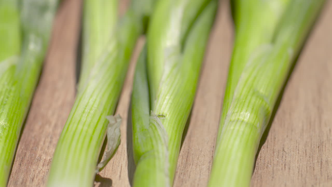 cierre la bandeja de un montón de cebollas verdes frescas descansando sobre una tabla de cortar de madera a la luz del sol