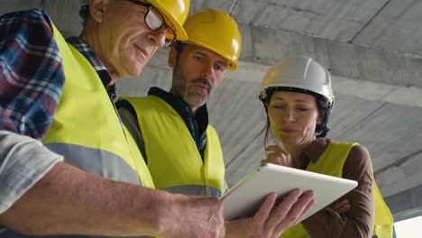 video estático de bajo ángulo de tres ingenieros caucásicos hablando en el sitio de construcción.