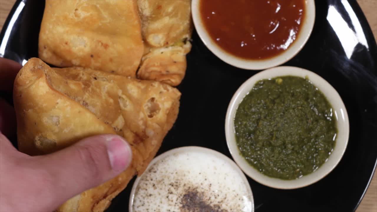 Top-shot track-in close-up of a hand grabbing a Samosa from a plate