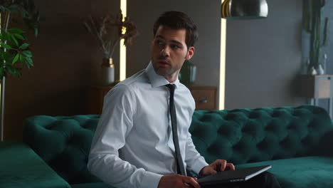 businessman closing laptop after work in office. worker sitting on sofa