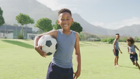 video portrait of smiling african american schoolboy holding football in field