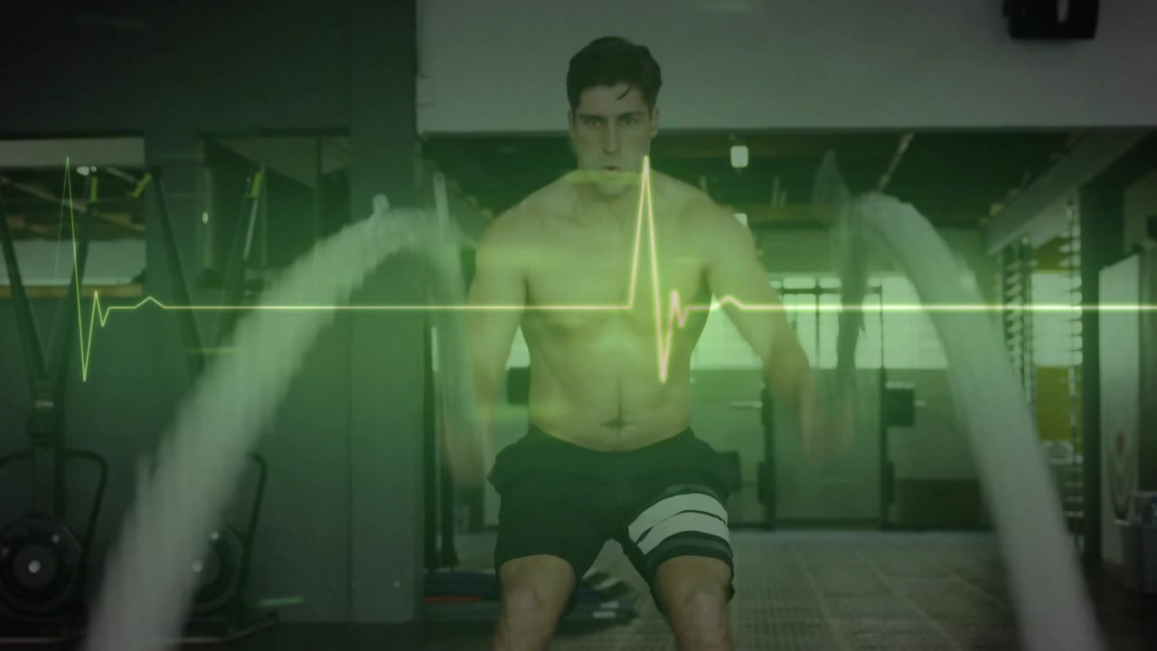 Uomo che afferra le corde e crea onde in palestra, eseguendo allenamento fitness con l'ECG che pulsa in sincronia.