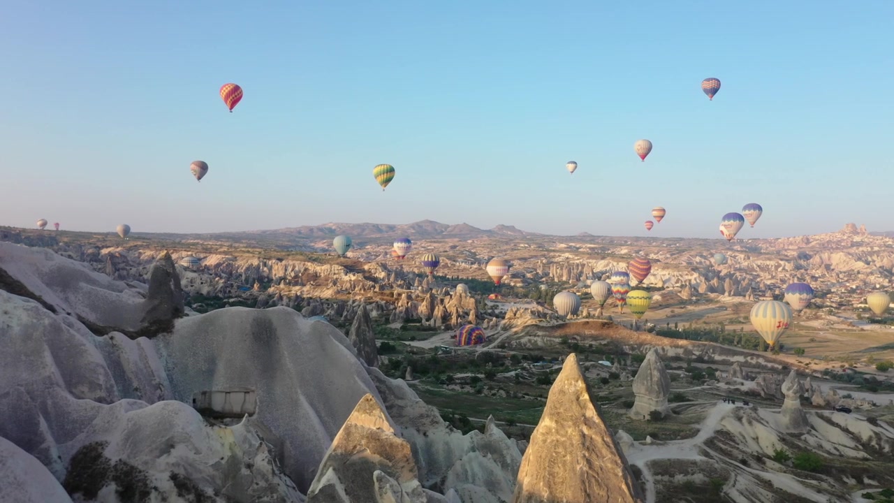 Vista aérea ampla de drone de múltiplos balões de ar quente flutuando pelo céu sobre a paisagem dramática do vale da Capadócia, Nevsehir, Turquia ao nascer do sol