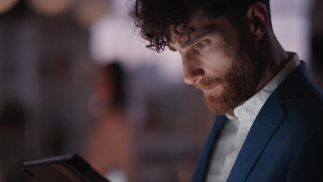 young businessman using tablet computer working late in office browsing information looking at data on digital touchscreen