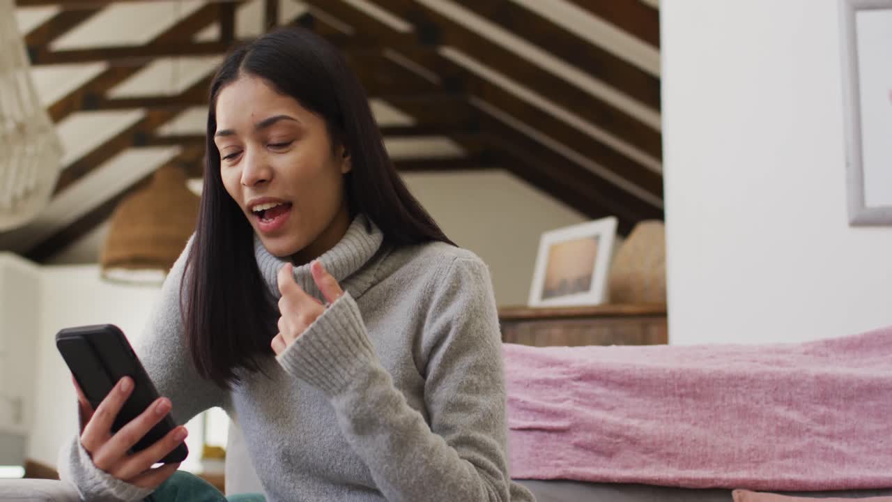 mujer biracial usando un teléfono inteligente y sonriendo en la sala de estar
