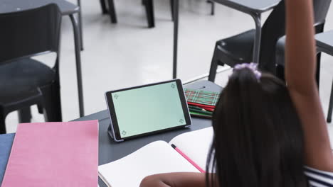 A-young-Asian-girl-with-long-black-hair-raises-her-hand-in-classroom,-copy-space