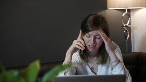 mujer profesional joven triste y molesta recibiendo malas noticias por teléfono en casa trabajando en la computadora portátil