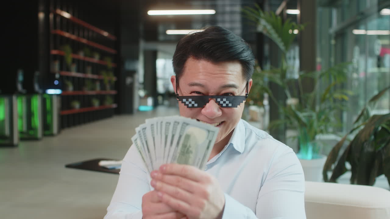 Un uomo d'affari ricco e maturo che indossa occhiali da sole da teppista che mostra soldi in dollari nella lobby di un ufficio moderno.