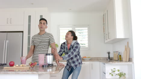 Feliz-Pareja-Gay-Diversa-Bebiendo-Batido-Y-Bailando-En-La-Cocina,-Copiando-Espacio,-Cámara-Lenta