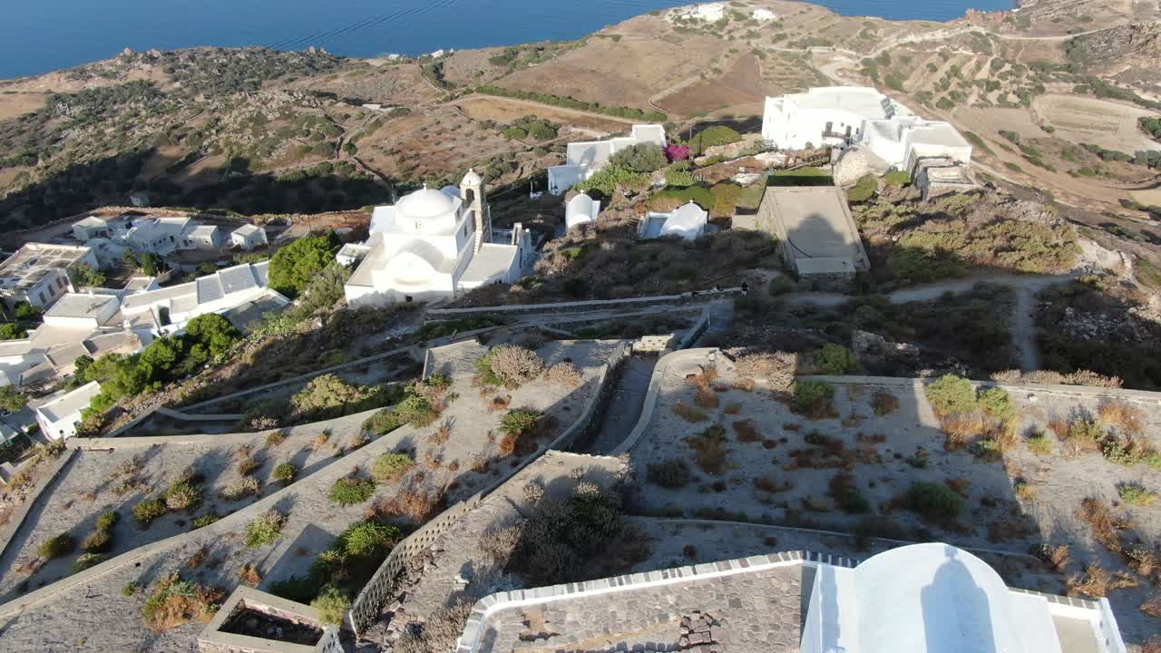 vista de avión no tripulado en grecia volando sobre una iglesia blanca en una colina con una casa blanca griega ciudad frente al mar azul en una montaña