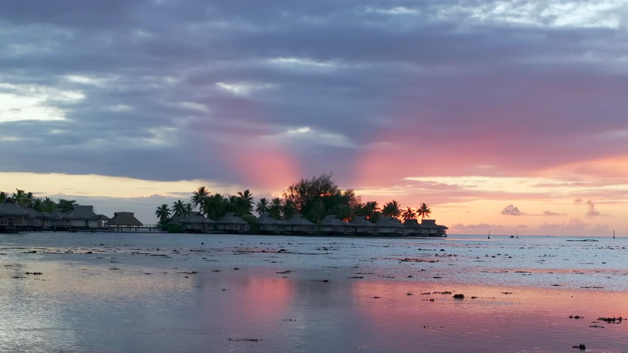 Stunning vibrant pink orange sunset sun rays Sofitel Kia Ora Resort Bungalow villas Moorea island French Polynesia aerial drone Cooks Opunohu Bay lagoon coral reef Pacific Ocean slide right motion