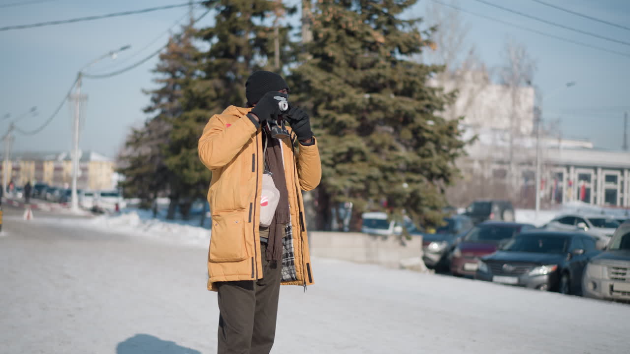 zoom in on photojournalist fix eyes on viewfinder adjusting lens and reviewing shot on lcd display against snowy urban street with blurred parked cars and frosted trees under bright winter sun