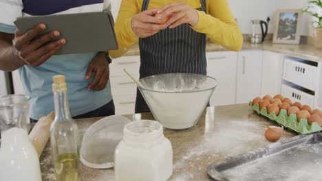 mid section of diverse couple using tablet and baking in kitchen