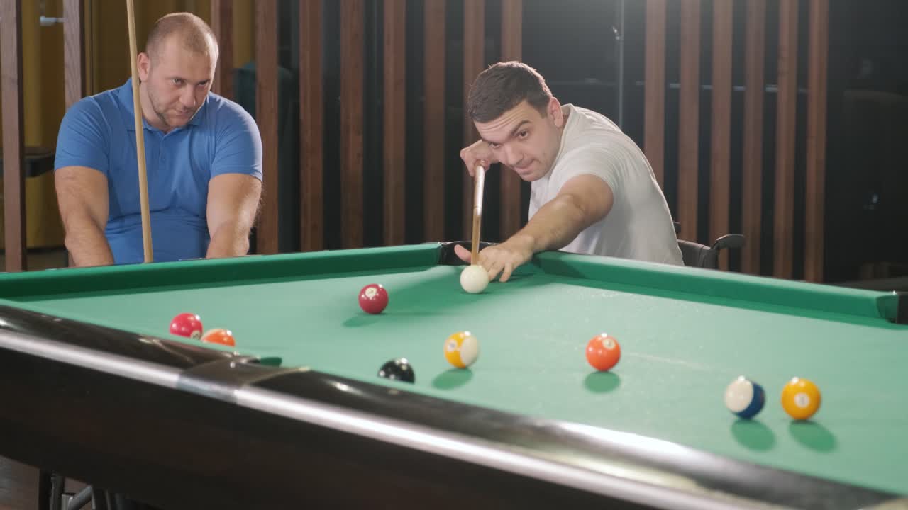 Adult men with disabilities in a wheelchair play billiards in the club