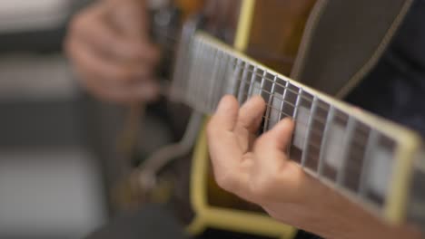 primer plano de un músico profesional tocando un solo en una guitarra eléctrica de cuerpo hueco con una púa de guitarra durante una sesión de grabación en un estudio con un fondo borroso