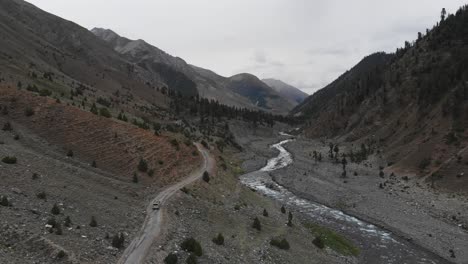 aerial drone follows van driving through alpine plain valley pakistani mountains