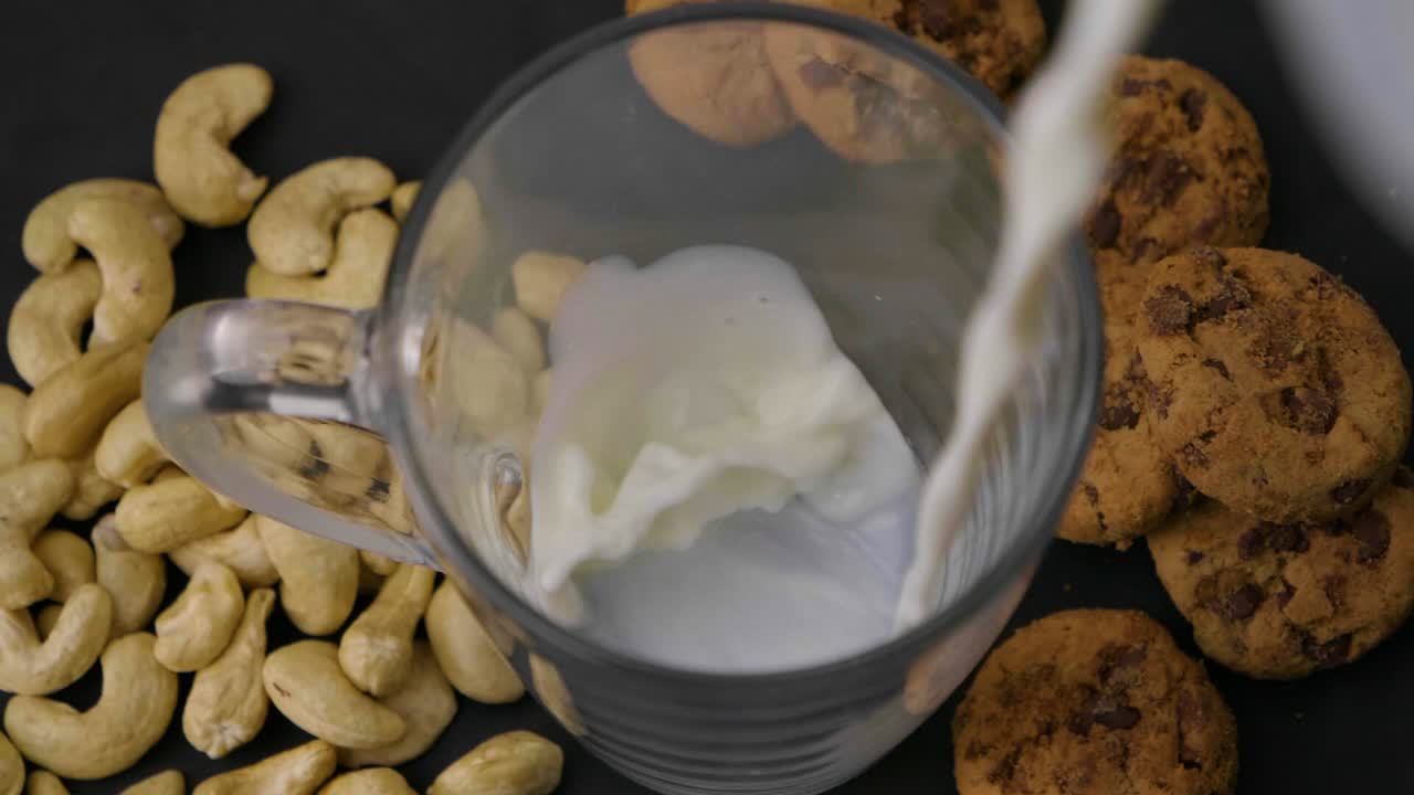 tiro de ojo de pájaro de un vaso en el que se llena la leche de avena vegana al lado hay nueces de cajú y galletas veganas para el desayuno