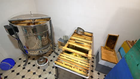 small room with working honey extracting machine. large metal box of frames waiting for pumping beside the centrifuge. high angle view.