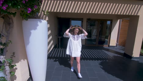 woman in a white dress and hat walking through a garden patio.