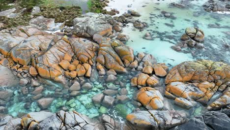 bright orange boulders along a coastline stand out against the clear blue water